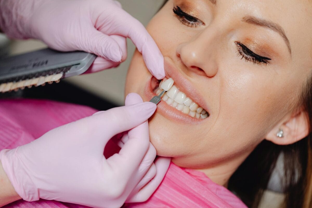 Family Cosmetic Dentistry Worcester: Smile Makeover Guide - Friendly Dental of Worcester Dentist in pink gloves compares a shade guide to the patient's upper front teeth during a cosmetic dental procedure.
