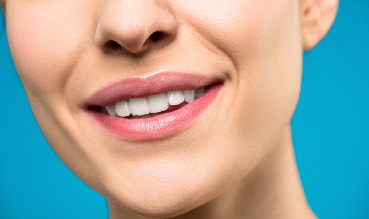 Family Cosmetic Dentistry Worcester - Friendly Dental of Worcester Close-up of a smiling woman's mouth showing white teeth and pink lips against a blue background.