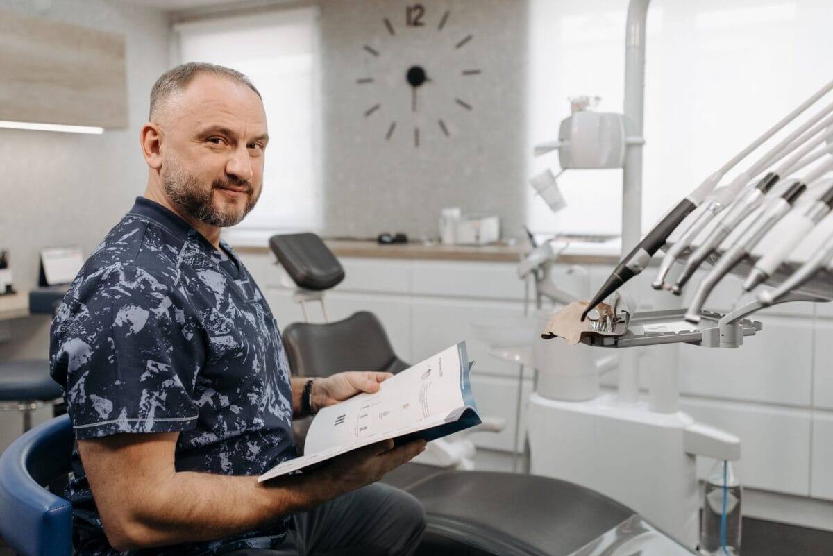 Family Cosmetic Dentistry Worcester: Transforming Lives One Smile at a Time - Friendly Dental of Worcester Dentist in a patterned blue scrubs sits in a dental clinic, reading a brochure.