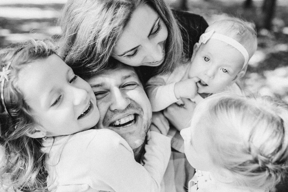 Family members—mom, dad, and two kids—sharing a warm, joyful hug in a black-and-white photo, smiling at the camera/each other.