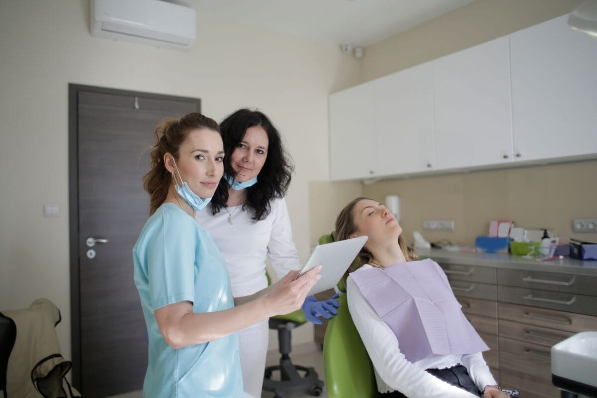 Smiling dentist in sterile mask and uniform showing tablet screen to assistant near patient in clinic Photo by Andrea Piacquadio on Pexels - Friendly Dental of Worcester Dental team in a clinic with a patient in a chair, posing for a photo during a checkup.
